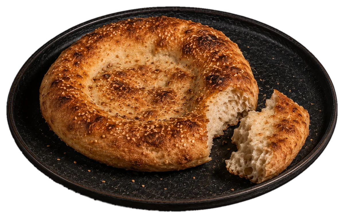 Round tandir bread with sesame, one piece torn off, on a black stoneware plate